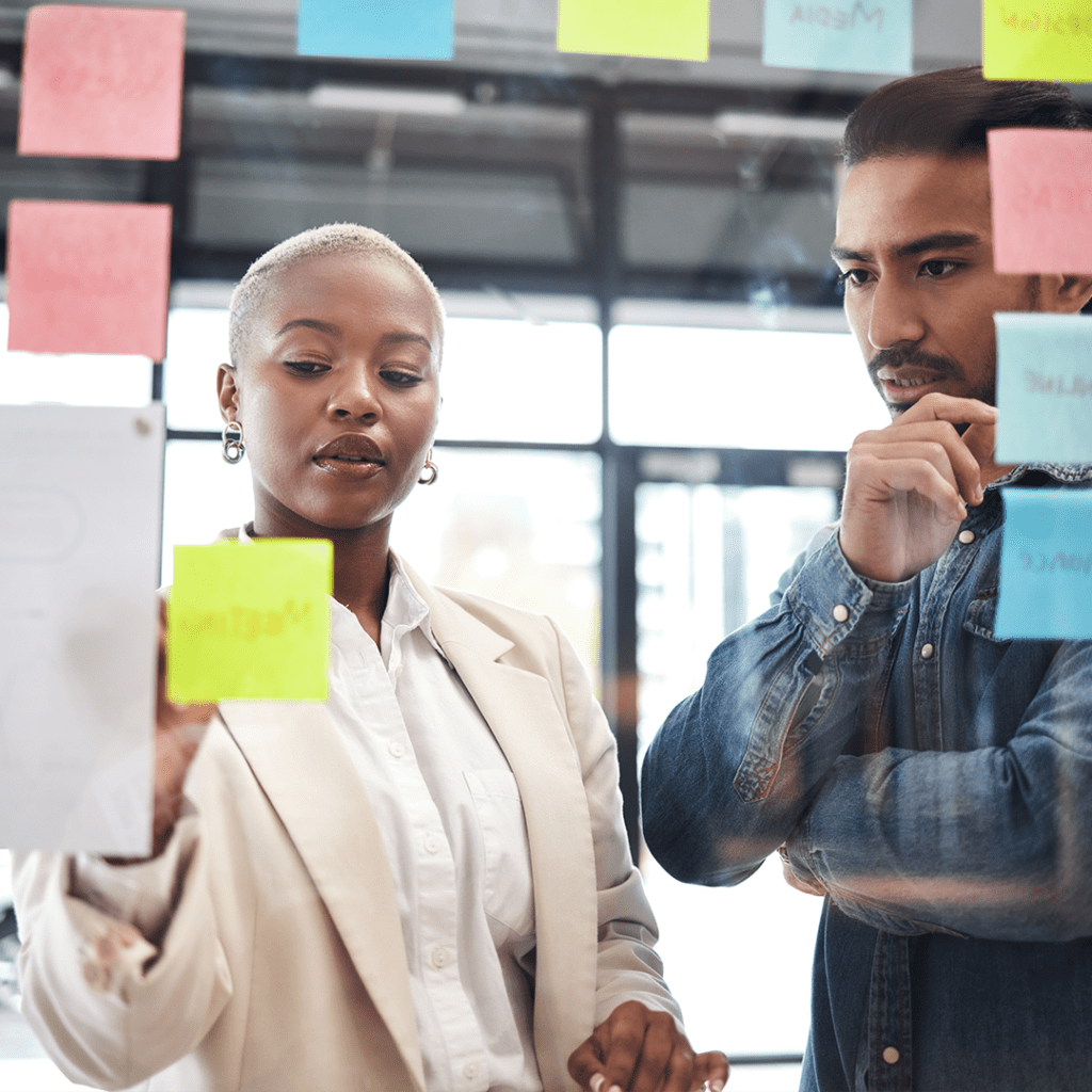 Website designer in discovery, strategy session. Woman and man writing on sticky notes placed on glass